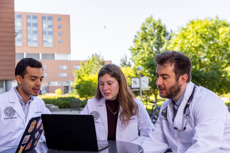 Three CU School of Medicine students sitting outside, looking at a computer.