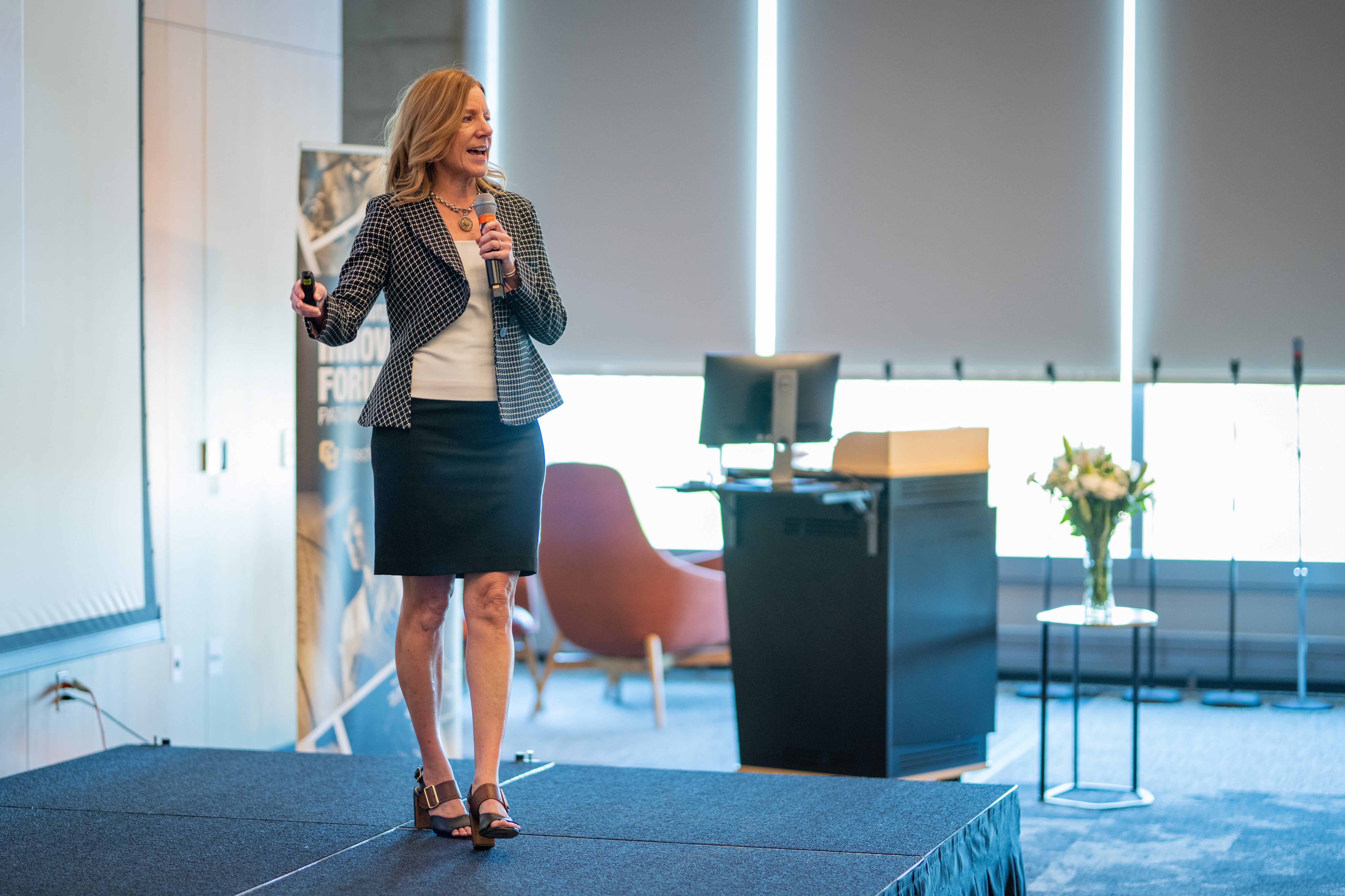 Tracy Bale presents on stage in the Elliman Conference Center in the Anschutz Health Sciences Building, mic in hand. 