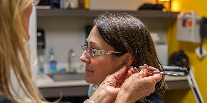 Licensed acupuncturist Dee Watts, left, applies a seed, a tiny metal bead, to the left ear of Cari Levy, MD.