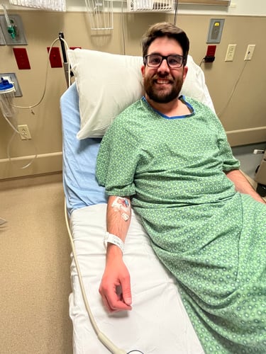 A man dressed in a hospital gown lies on a hospital bed with an IV in his arm.
