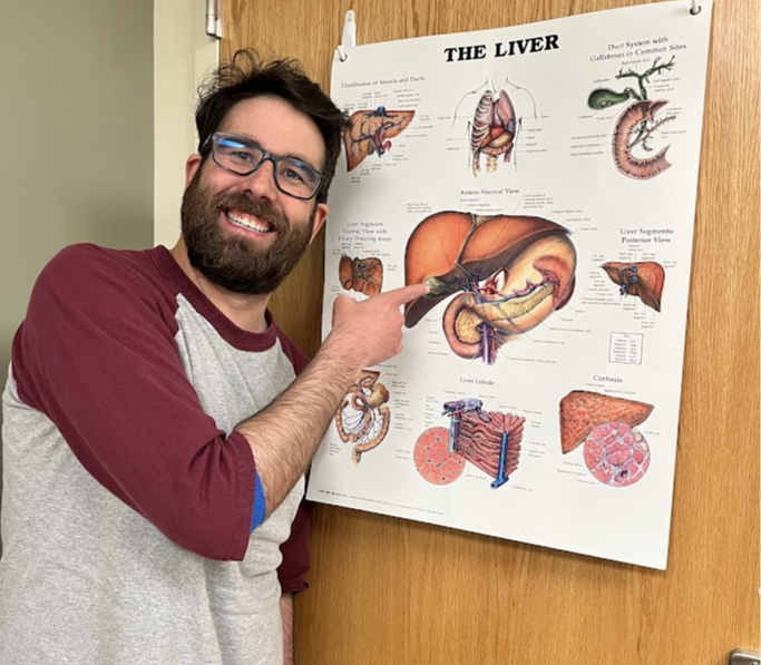 Bobby Click smiles while pointing to a poster of a liver on a door.