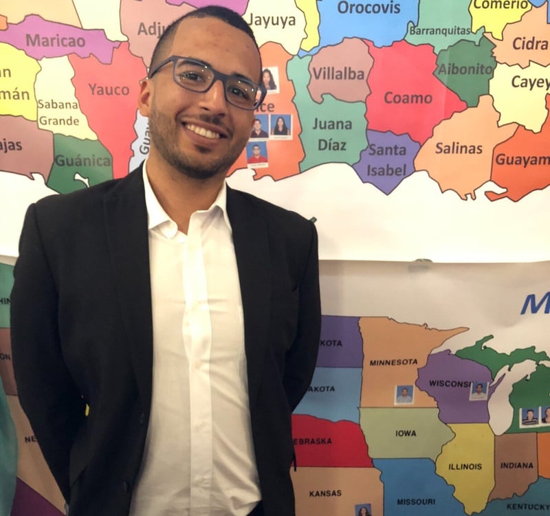 Anthony Robateau Colón smiling in front of a map. 