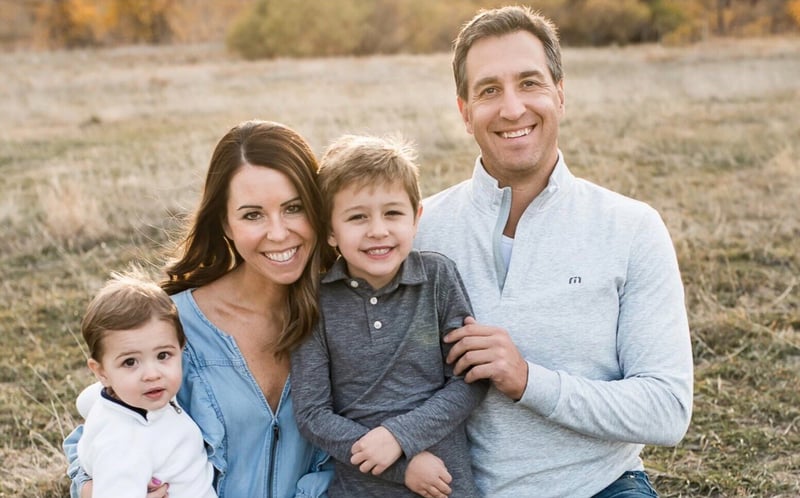 Colleen smiling with her husband and two sons as they sit on grass outside.