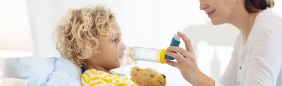 Parent helping child to use an asthma inhaler with spacer.