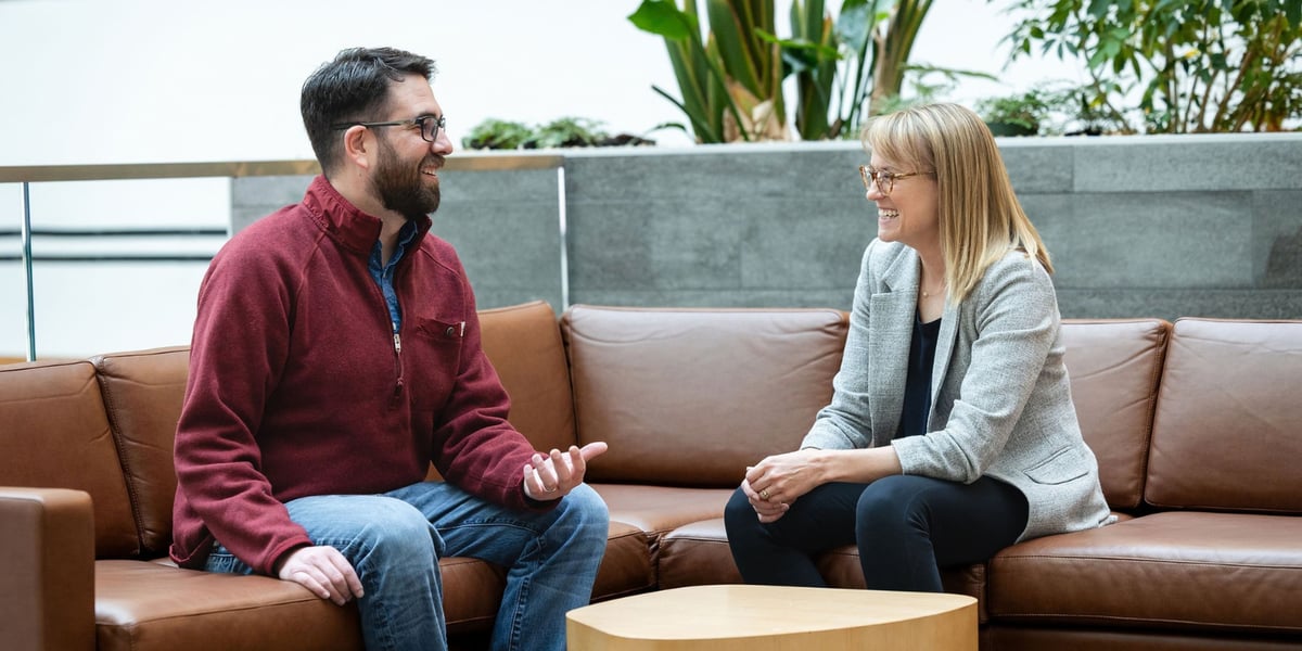 Bobby Click, wearing a red pullover, smiles while talking with Whitney Jackson, MD, as they sit on a brown couch at CU Anschutz.