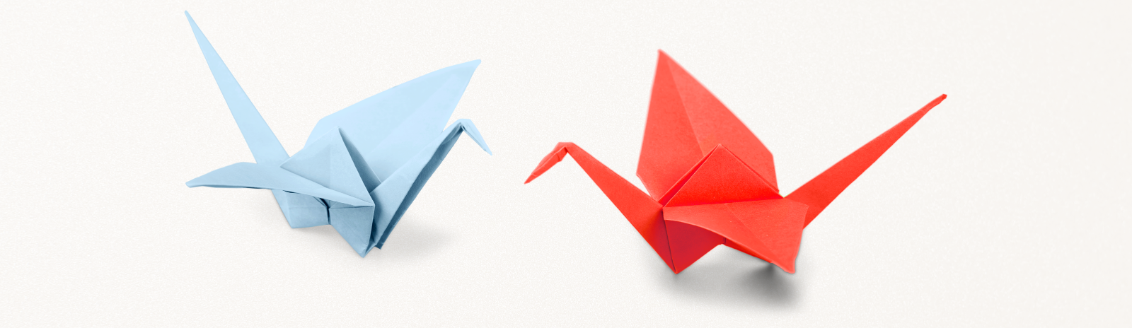 Two small paper cranes, one made of light blue paper and the other is red.