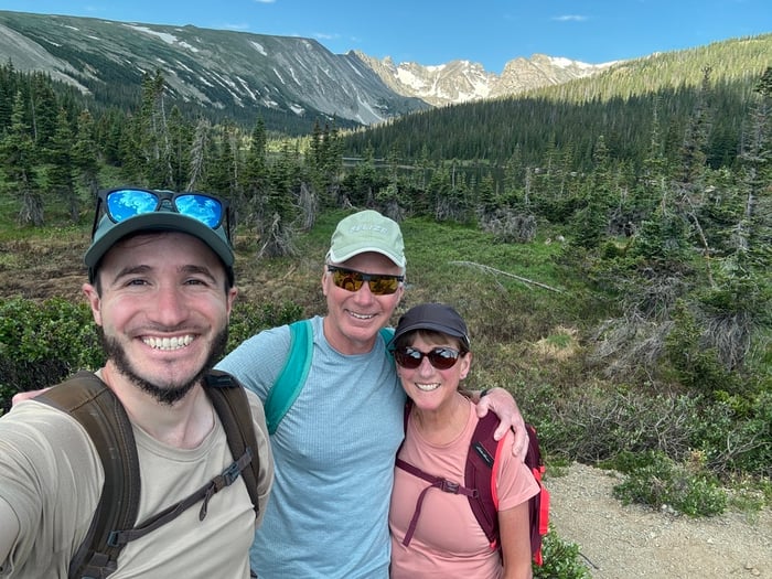 Three people smiling while standing in a forest.