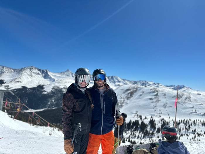 Two people smiling at a ski resort while holding skis.