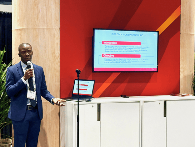 Isaac Acquah, wearing a blue suit and tie, speaks into a microphone while presenting research at a national conference.