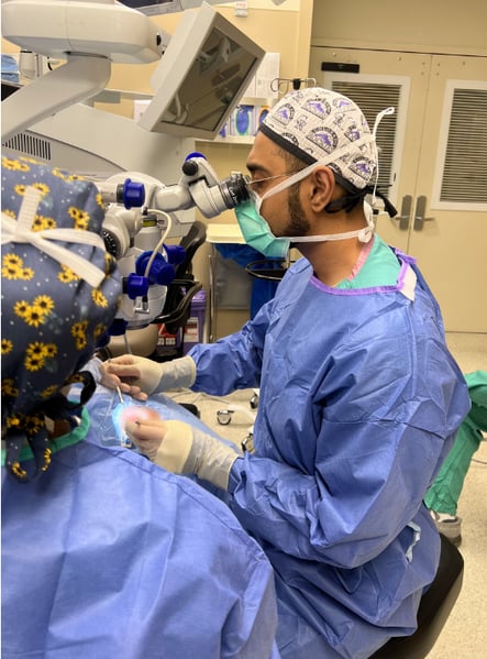 Image of a man wearing scrubs conducting surgery on an eye.
