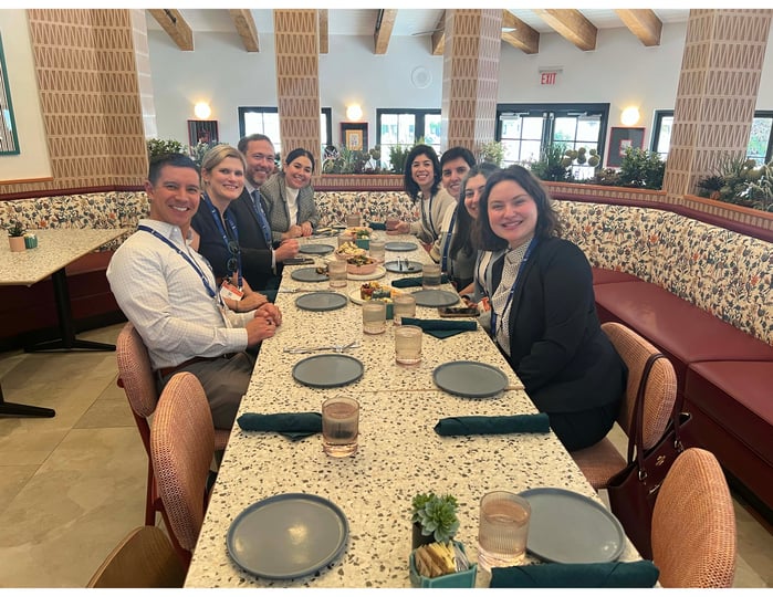 Eight people sit at a long table and smile for a photo.