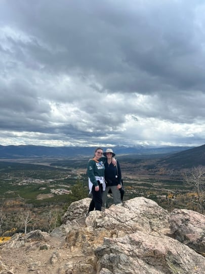 Two adults smile while hiking in the mountains on a cloudy day.