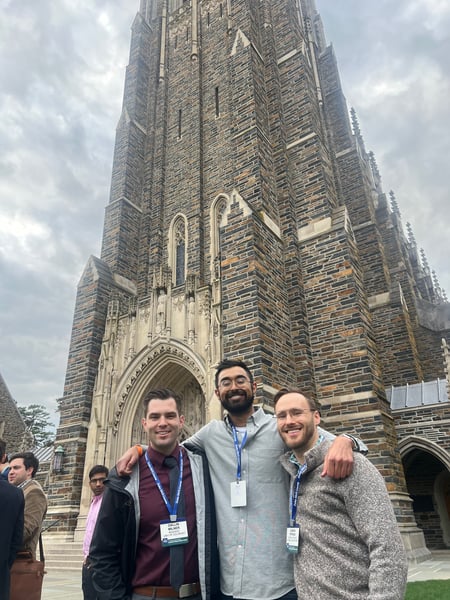 Three men smile in front of a church.