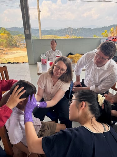 Three adults examine a pediatric patient as they sit in a chair outside. Two of the adults have purple gloves on and are touching the patient's face.