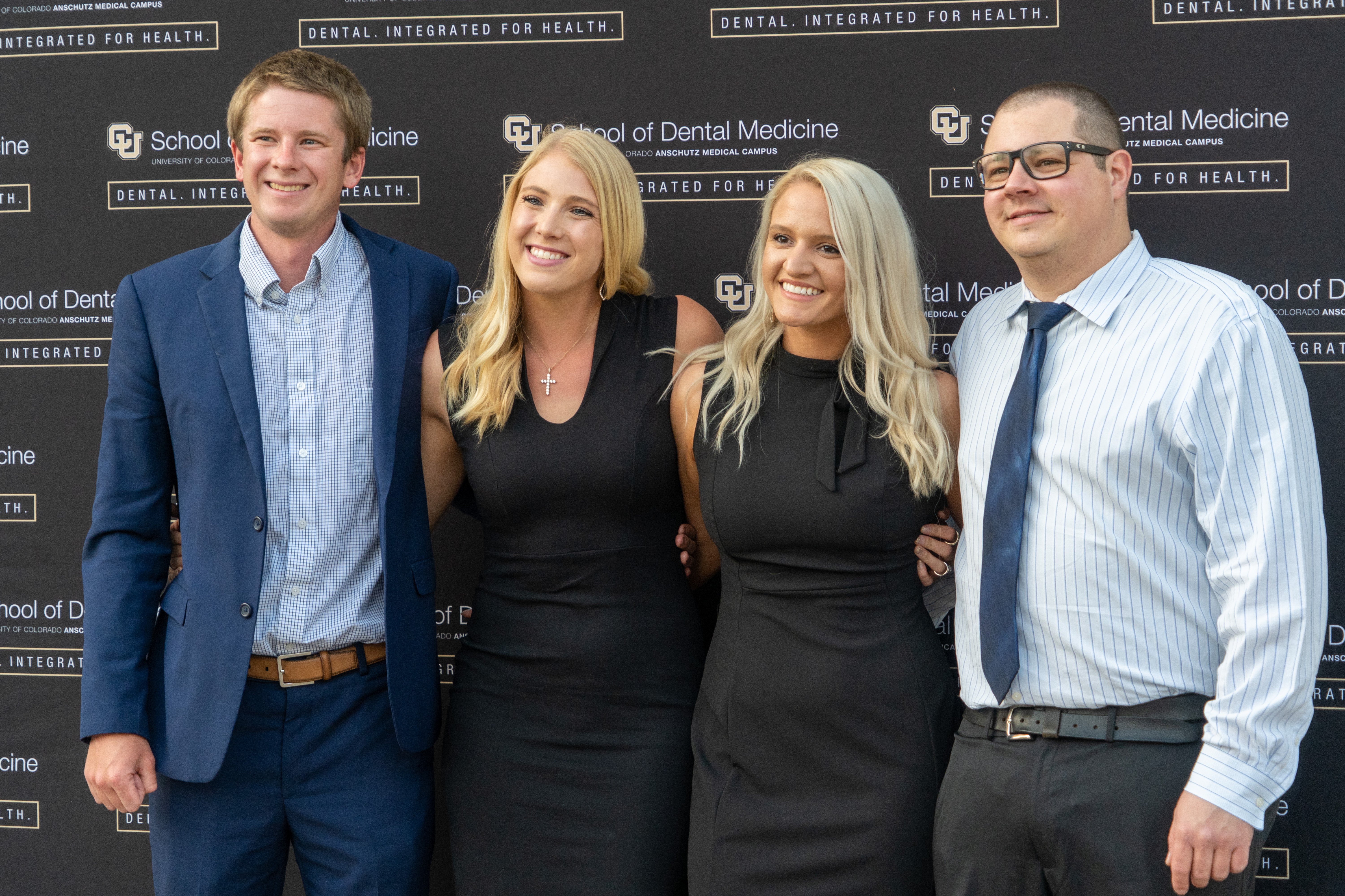 four people standing together in front of a black backdrop