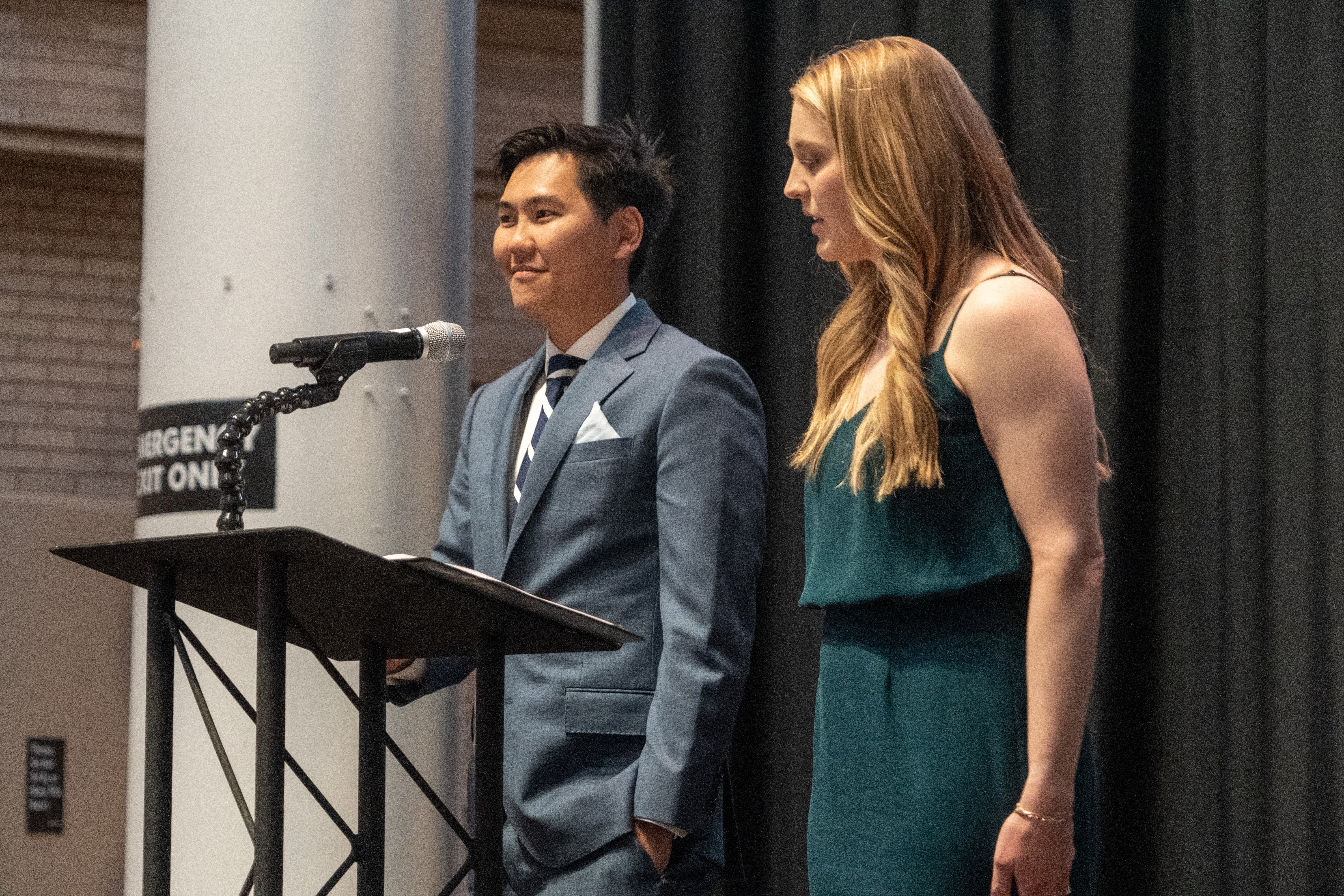 two students speaking at a podium on a stage inside