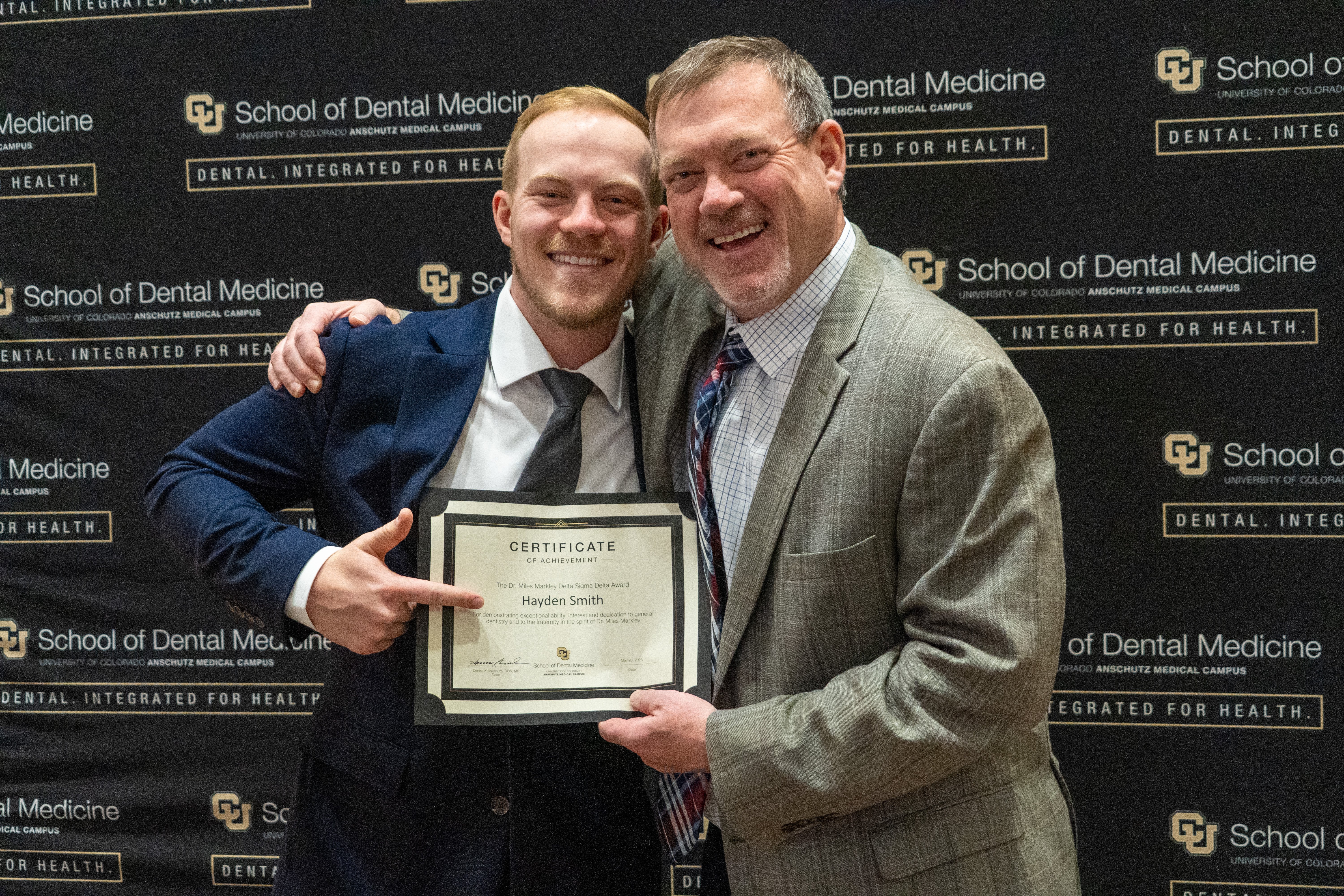 two people standing together with a certificate in front of a black backdrop