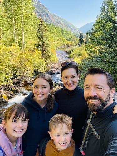 Julie Venci, MD, smiles with her husband and three children while walking by a creek in the mountains.