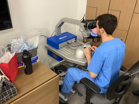 Ophthalmology resident in blue scrubs uses a surgery simulator to practice a cataract removal surgery.