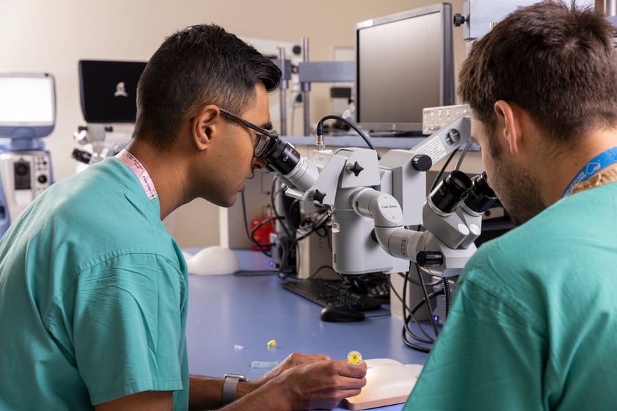 Two men wearing scrubs look into a microscope as they practice surgical techniques.