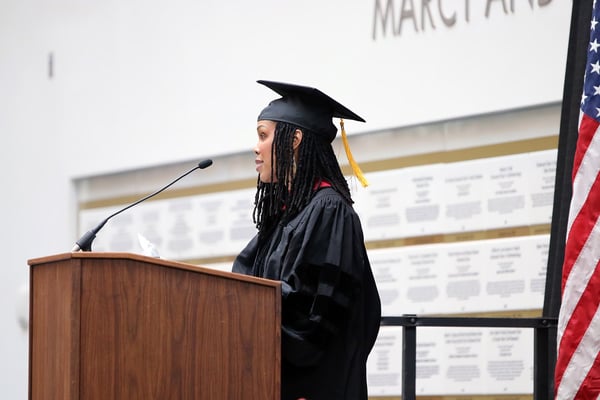 Dr. Blackstock gives her address in a cap and gown at a podium.