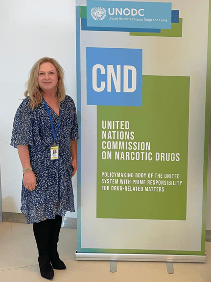 Dr. Jacci Bainbridge standing next to a United Nations Commission on Narcotic Drugs banner.