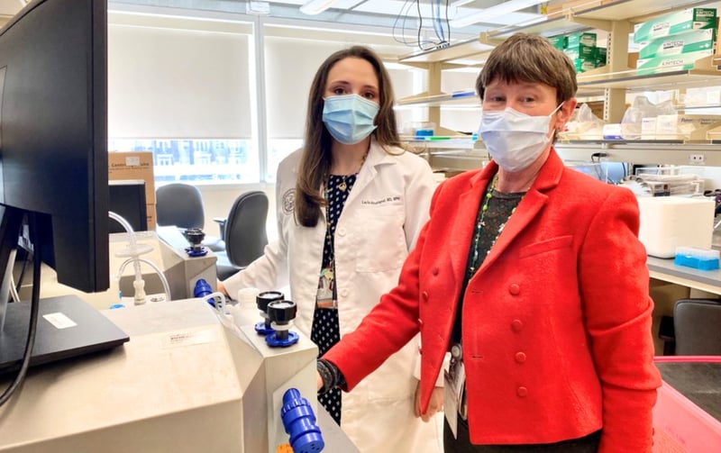 Two researchers wearing masks pose for a photo while standing in a lab.