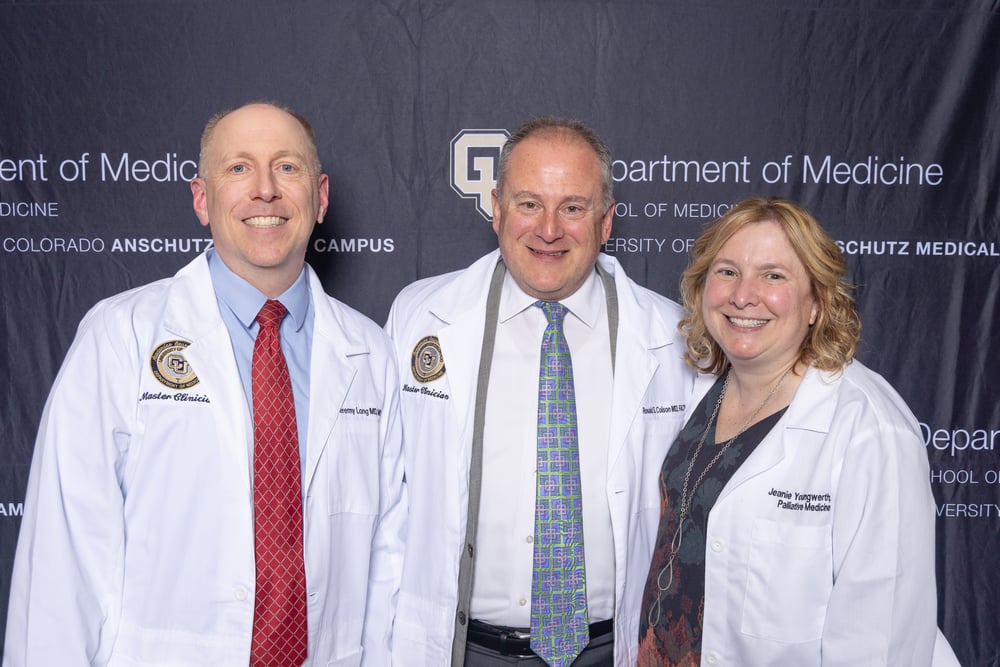 Two men and a woman, all wearing their white coats, smile beside one another in a group photo.