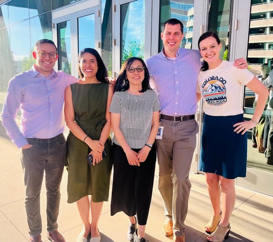 A group of five people smiling while standing outdoors.