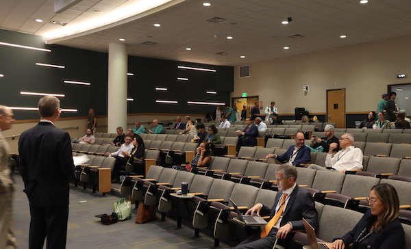 Dr. McIntyre stands in the front of an auditorium with people sitting in chairs