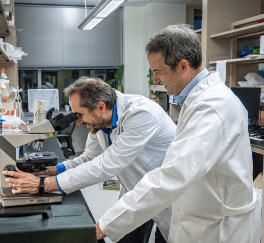 Bitler looks into a microscope as Bitler stands next to him.