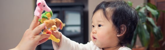 Adult hand with finger puppets playing with baby.