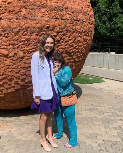Kimberly Christnacht, wearing her white coat over a purple dress, smiles with her sister, who is dressed in blue.