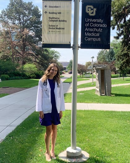 Kimberly Christnacht wears her white coat while standing outside underneath a sign for the University of Colorado Anschutz Medical Campus.