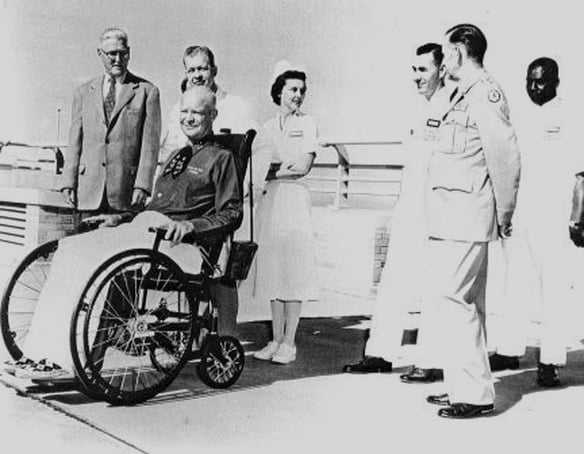 Historic photo of Dwight Eisenhower in a wheelchair surrounded by medical staff.