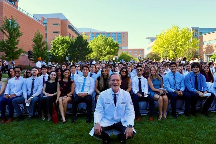Dean John H. Sampson, MD, PhD, MHSc, MBA, kneels and smiles with members of the Class of 2030 during their Matriculation Ceremony.