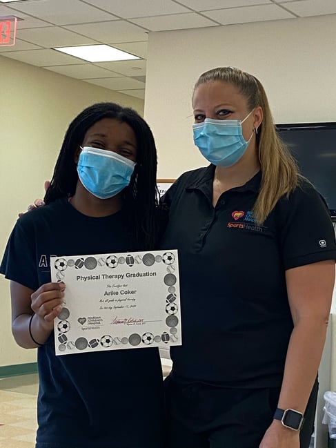 Arike Coker smiles while standing next to physical therapist