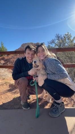 Kines and her husband kneel down to hug their fuzzy dog at the base of a hiking trail in Moab, Utah.