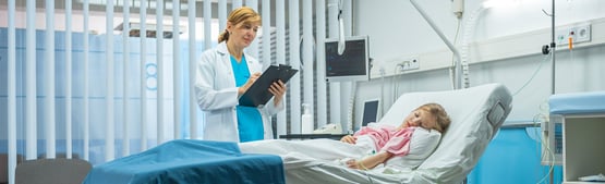 Stock image of doctor reviewing chart of child in hospital bed.