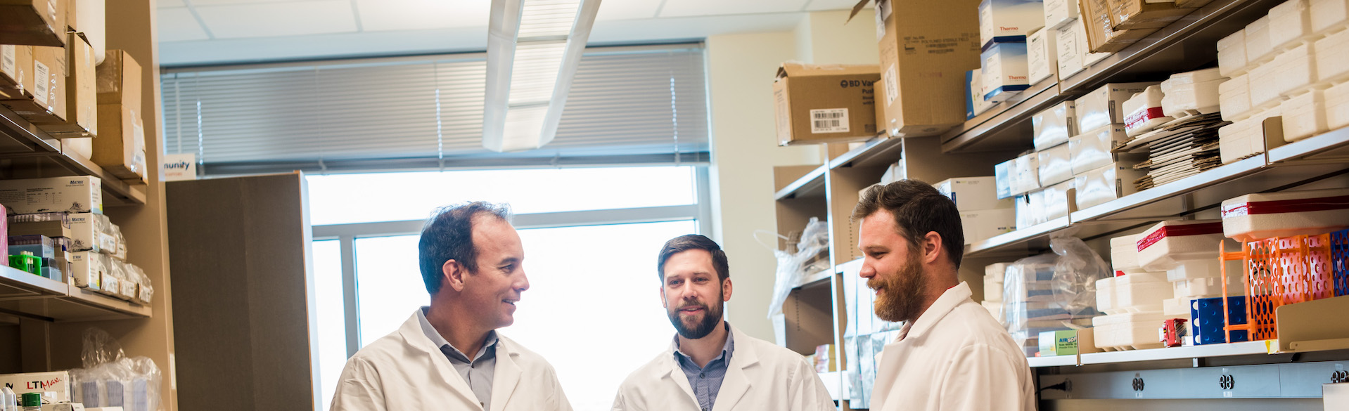 Three scientists wearing lab coats and standing in lab. 