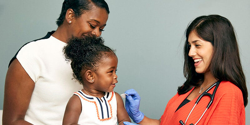 Little girl sitting on mother's lap to receive vaccination from doctor