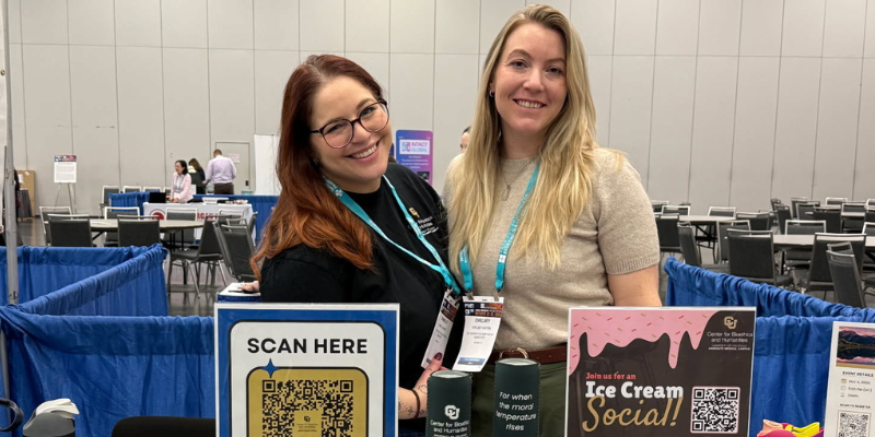 CBH Pperations Manager Danielle Chaet and Director of Clinical Ethics Chelsey Patten smile behind CBH exhibit table with giveaways and sign promoting ice cream social