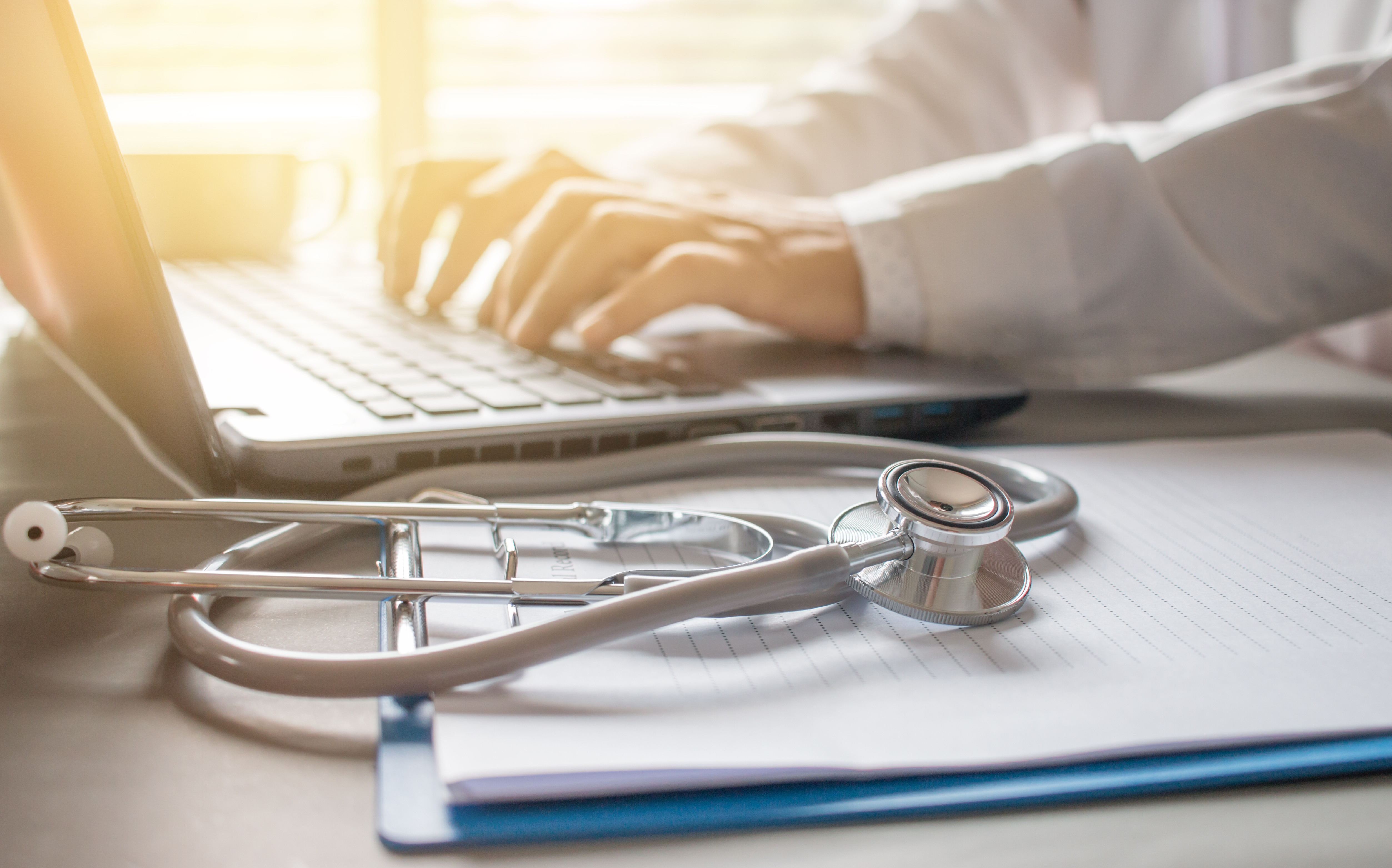 Person typing with stethoscope in foreground