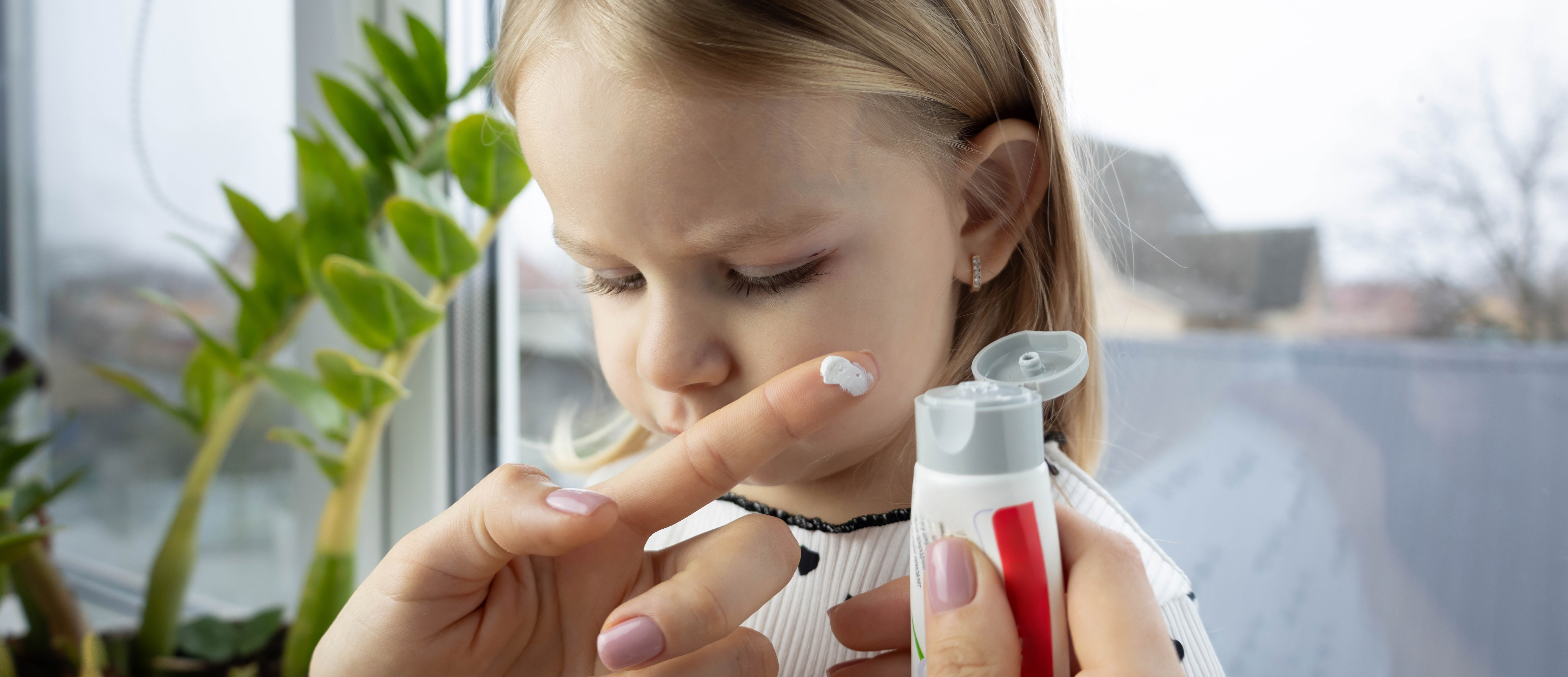 Person holding cream tube in front of female child's face. 