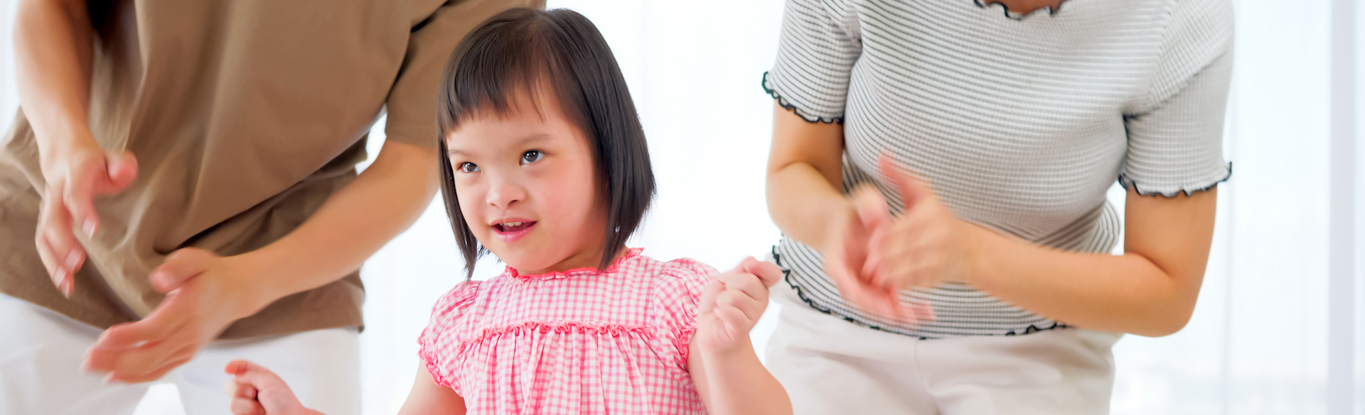 Image of smiling child with Down syndrome walking in front of two adults.