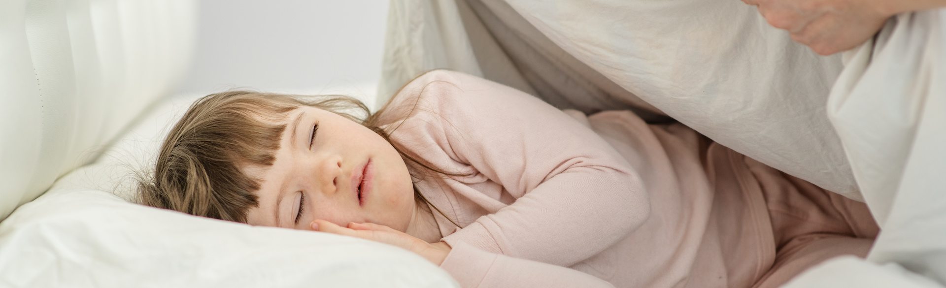 A sleeping young woman with Down syndrome is being tucked into bed.