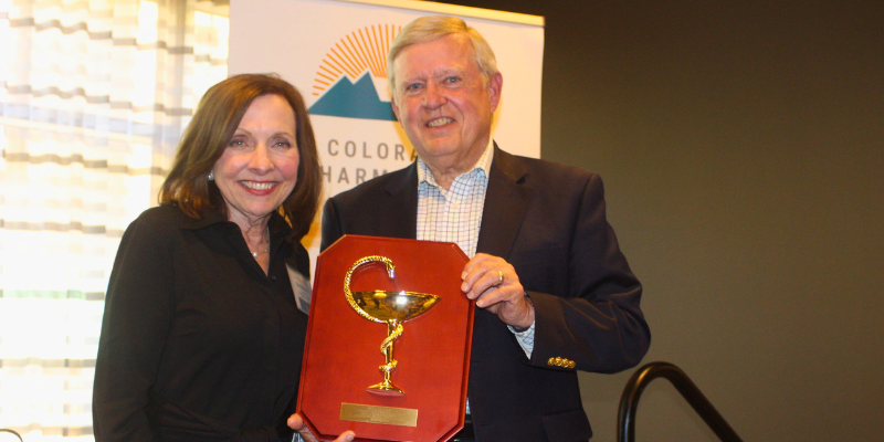 Two people hold a Bowl of Hygia award plaque and smile at a Colorado Pharmacists Society event.