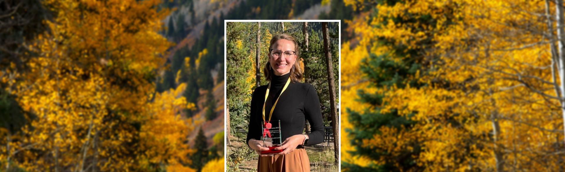 Erin Burke-Leaver holding award, fall foliage in background