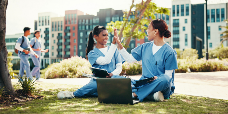 nursing students high-five outside with computer
