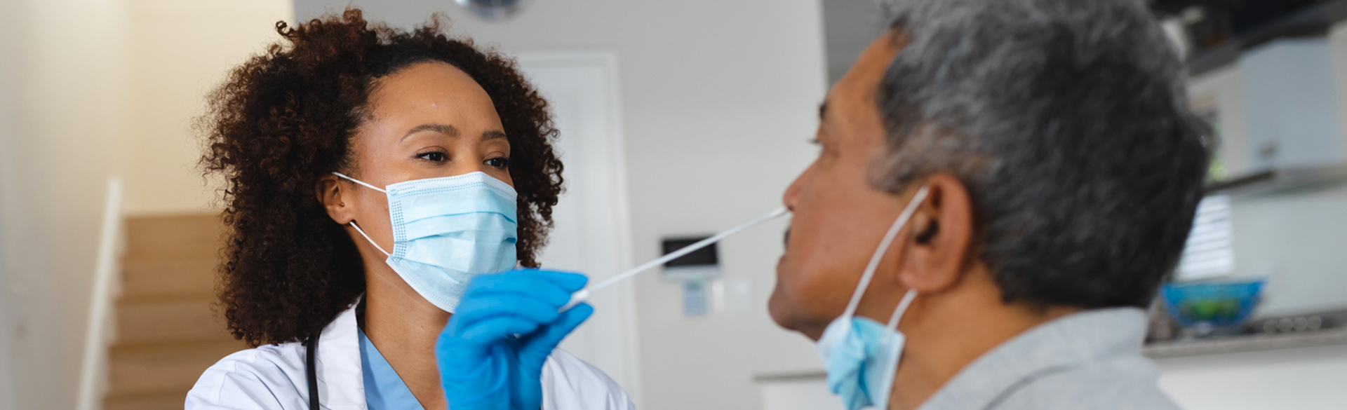 A masked and gloved healthcare provider begins a nasal swab on a patient for a COVID test